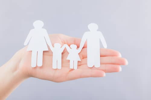 Paper cut outs of two adults and two children holding hands to illustrate the family unit.