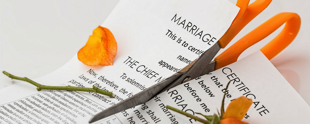 A pair of orange scissors cutting up a marriage certificate.