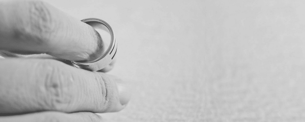 A black and white image of someone holding a wedding ring between two fingers.