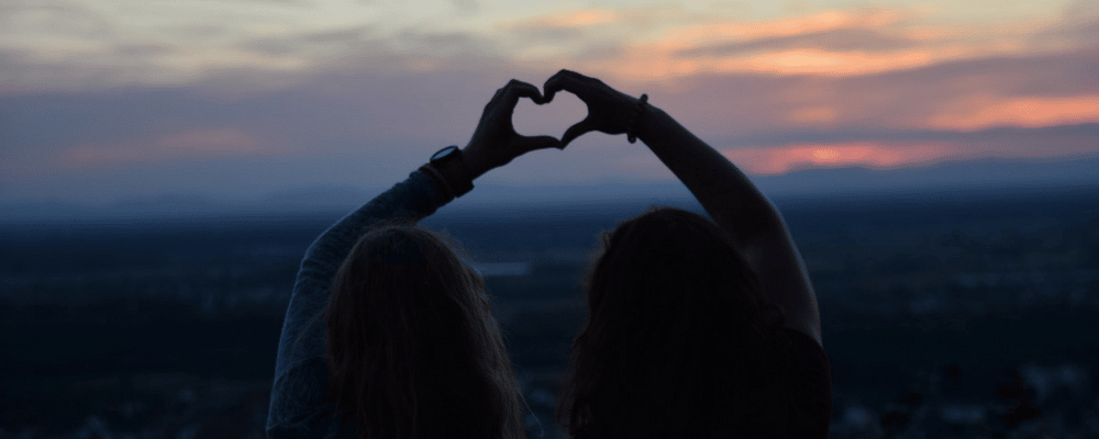 Silhouette of two people forming a heart shape with their hands.