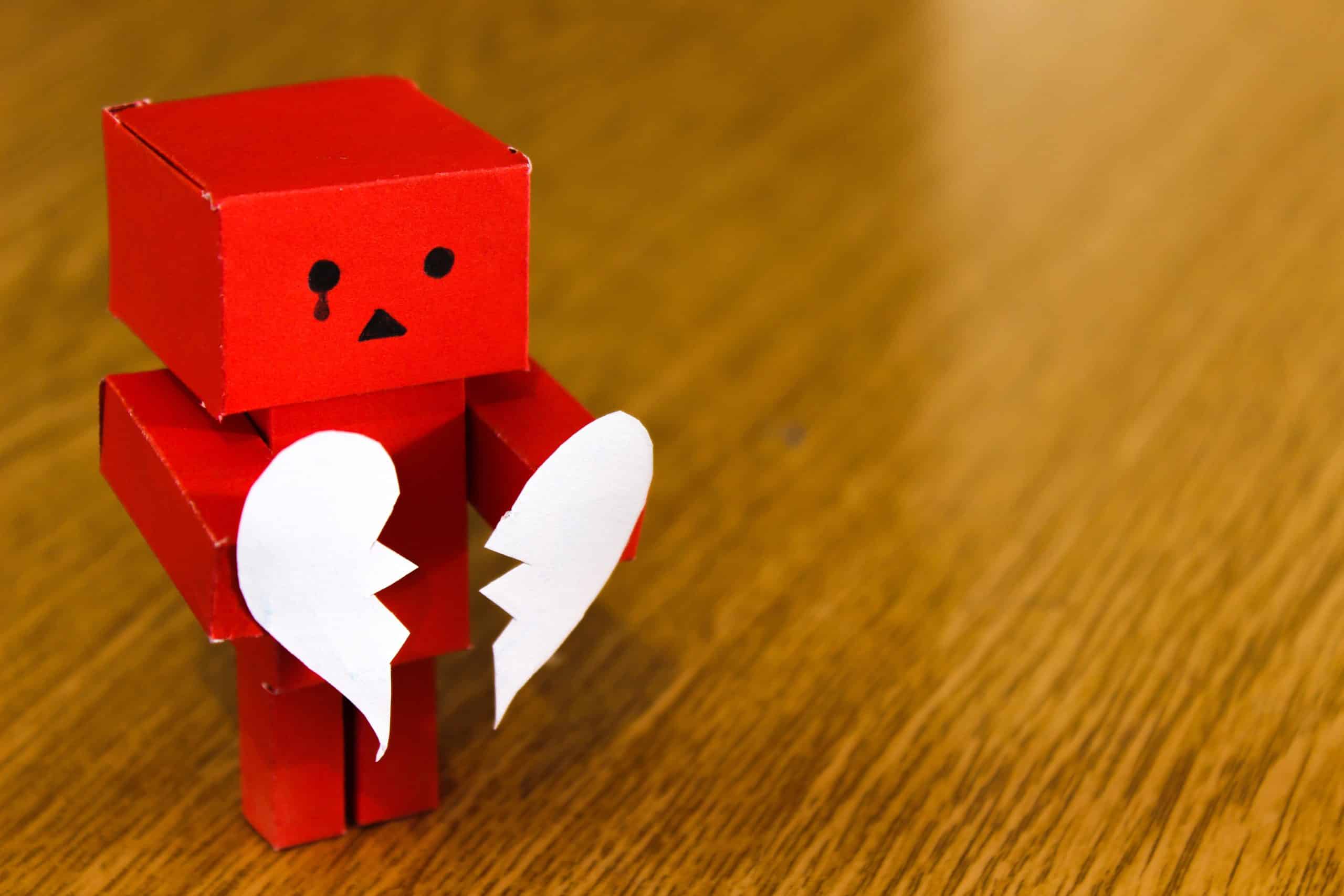 A sad cardboard figure holding a white broken heart