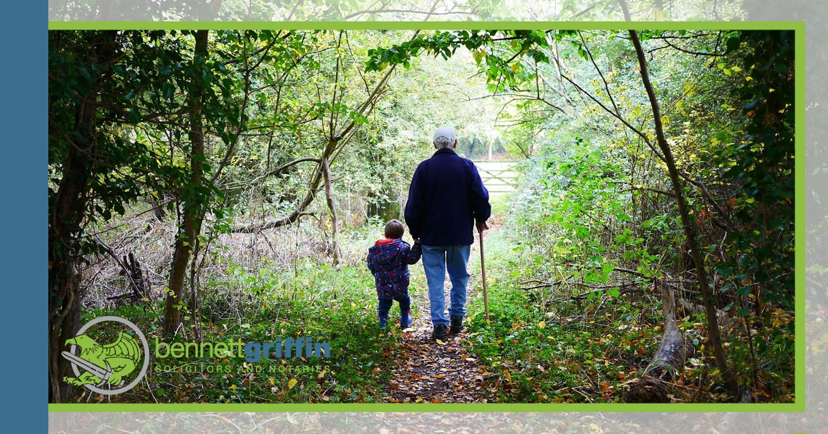 An older person walking with a young child in woodland