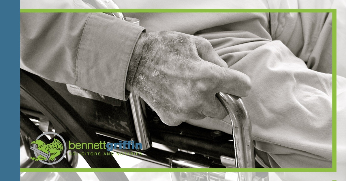An elderly person in a wheelchair, holding onto a hand rail.