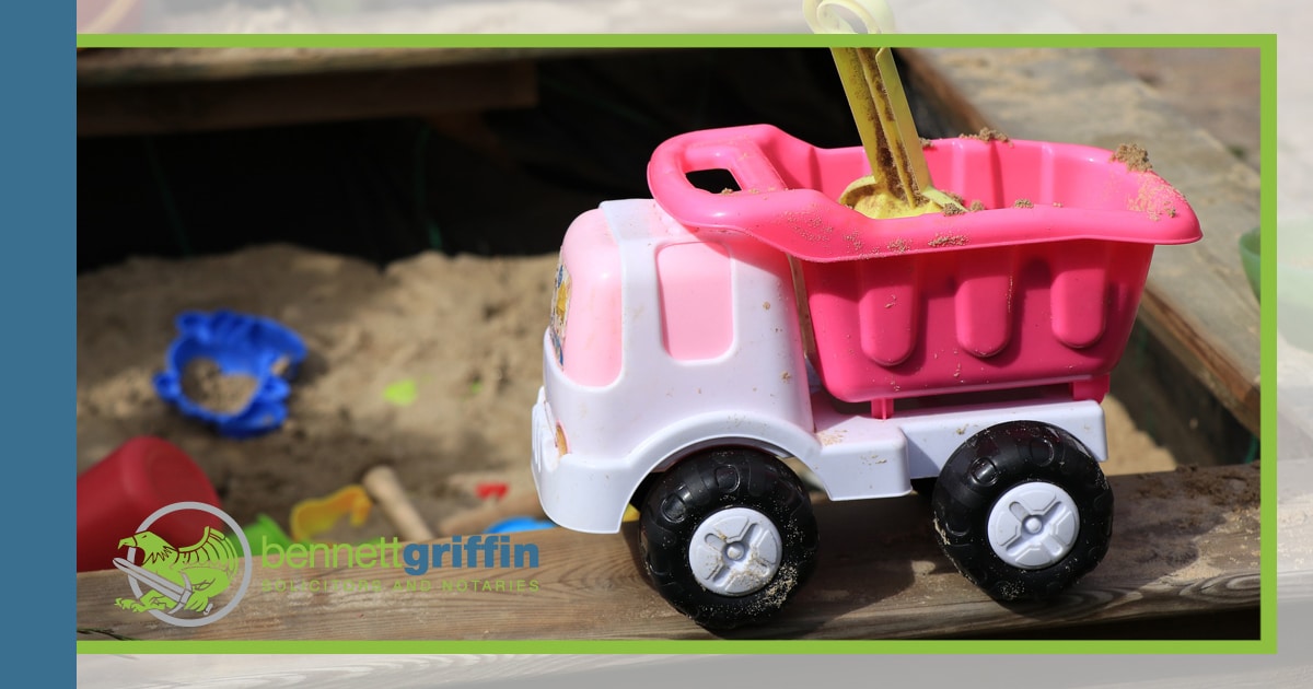 A childs toy dump truck with a childs sand pit in the background.