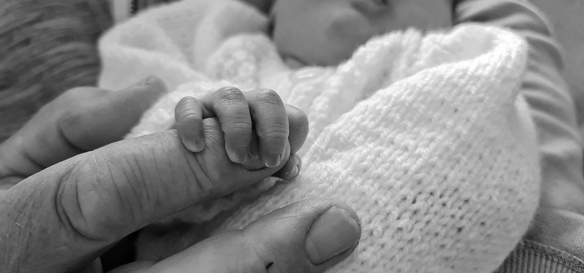 Newborn baby's hand gripping an adult's finger.
