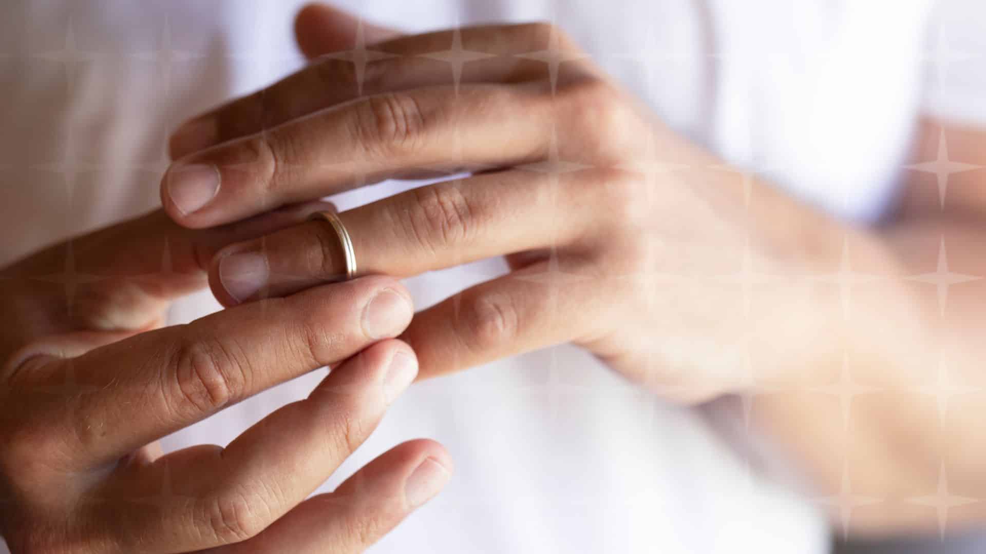 a pair of hands removing a wedding ring.