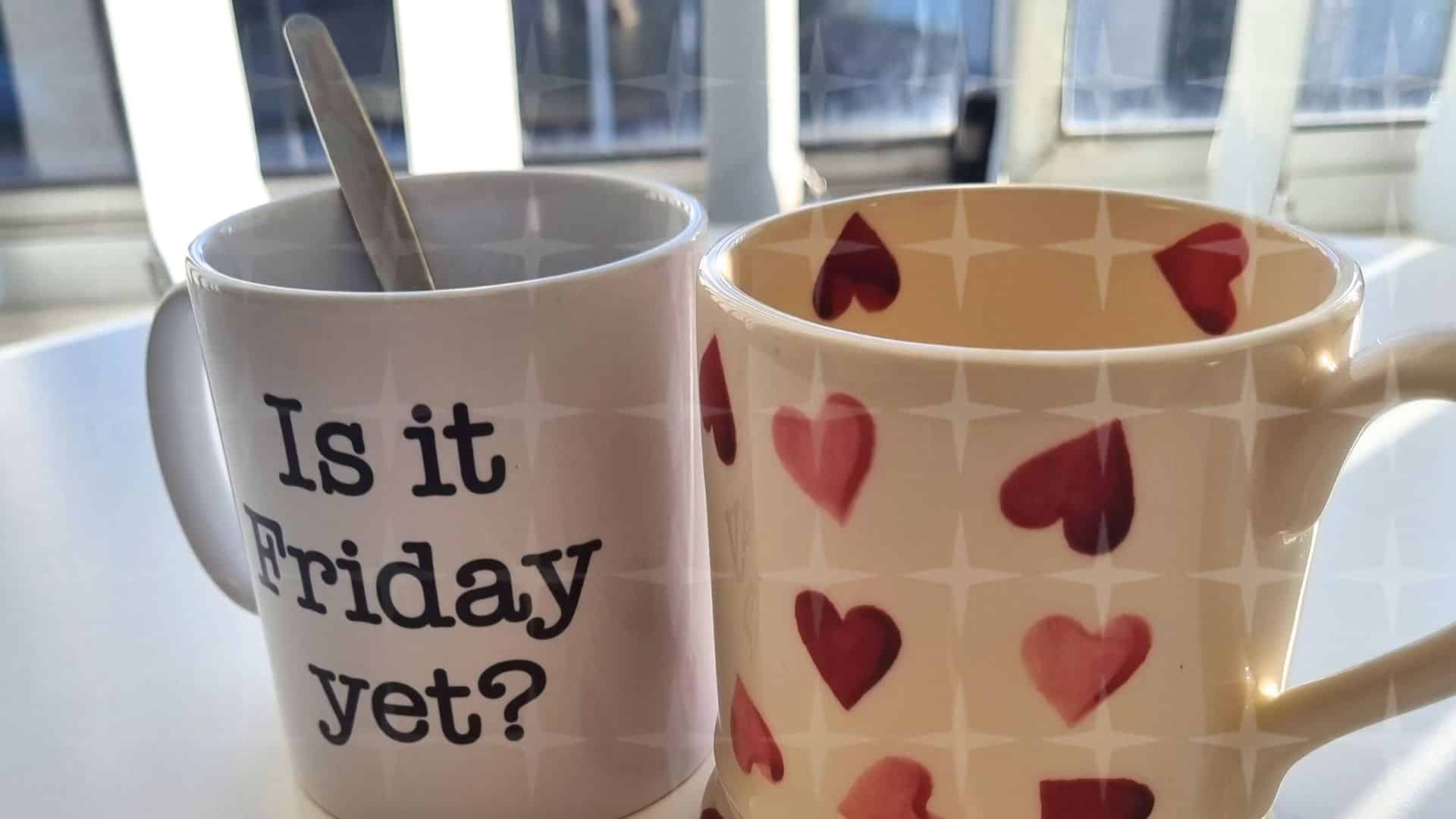 Two coffee mugs on a kitchen table side by side. One is white with red hearts.