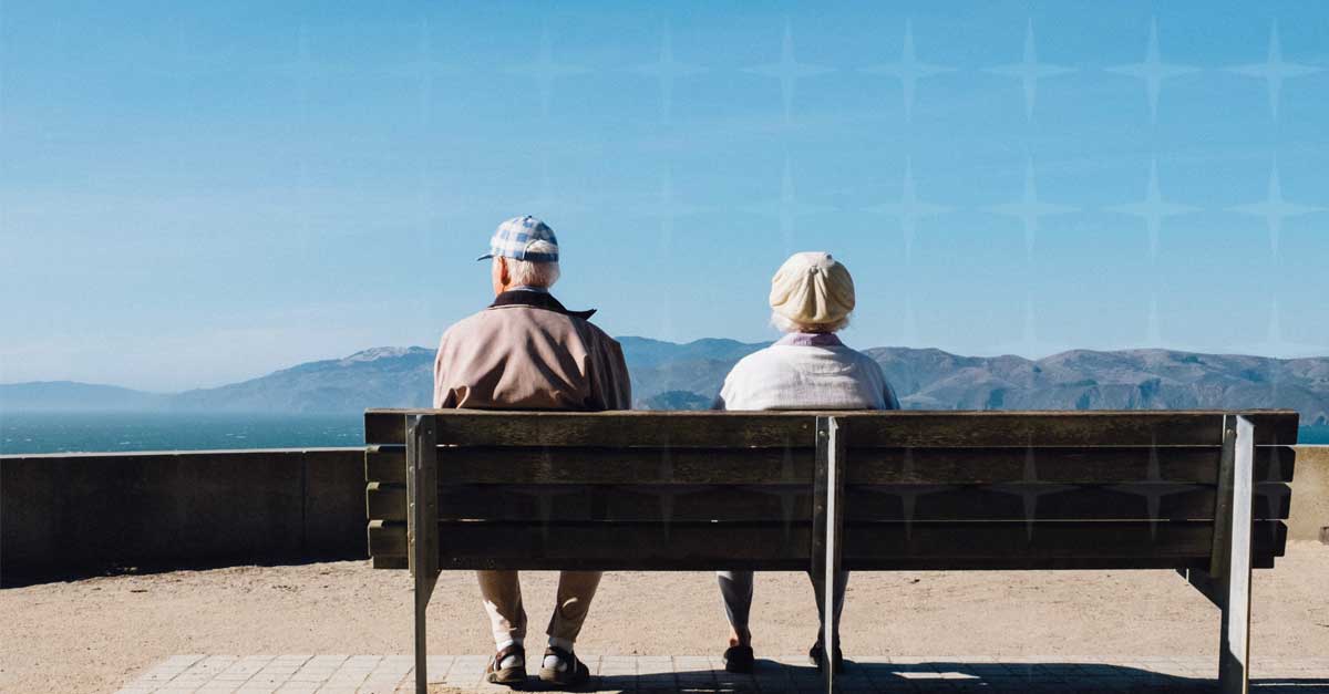 An older couple sitting on a bench, looking out on the view.