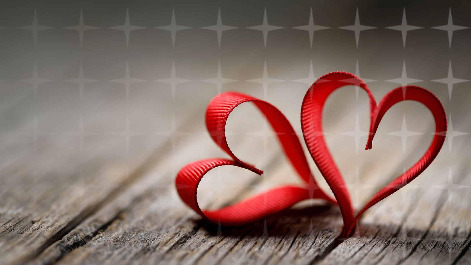 Two red ribbons in the shape of a heart resting on a wooden table.
