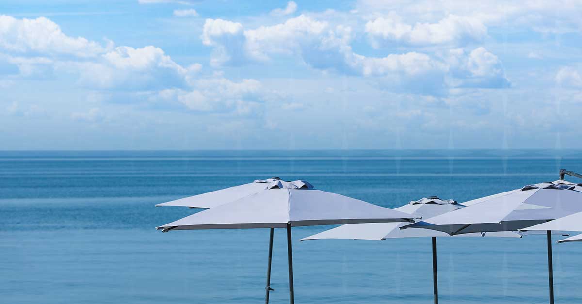 A view of the horizon with the ocean. Close by are some white parasols to indicate a place to sunbathe and relax.